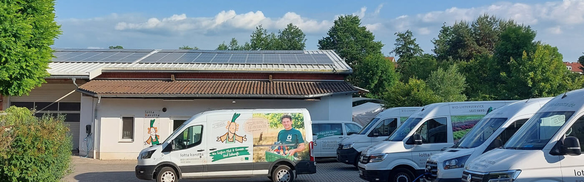 KI generiert: Mehrere Lieferwagen stehen auf einem Hof vor einem Gebäude mit Solarpanelen. Ein Van trägt ein Bild und den Text:
"lotta karotta biokiste."