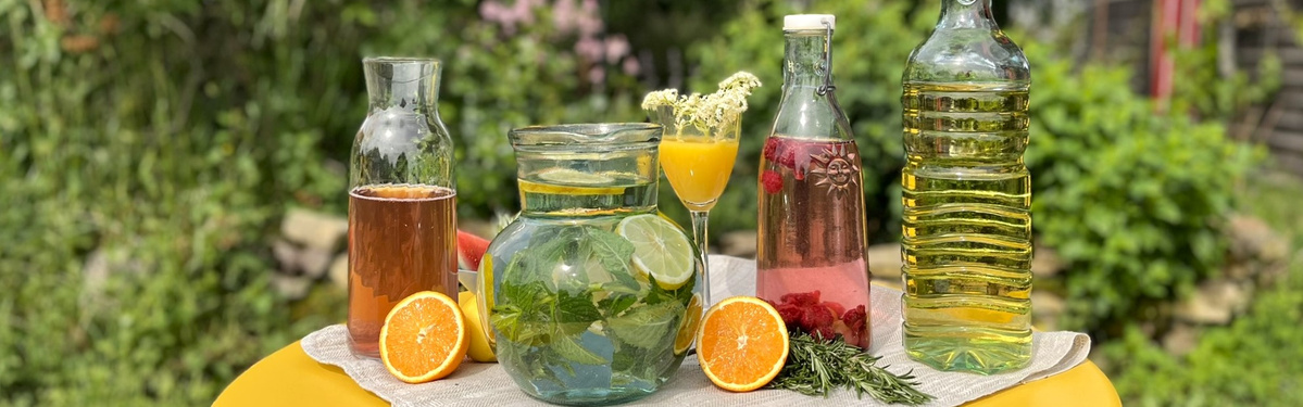 KI generiert: Verschiedene Glaskaraffen mit bunten Getränken und Zitrusfrüchten auf einem Tisch im Freien.