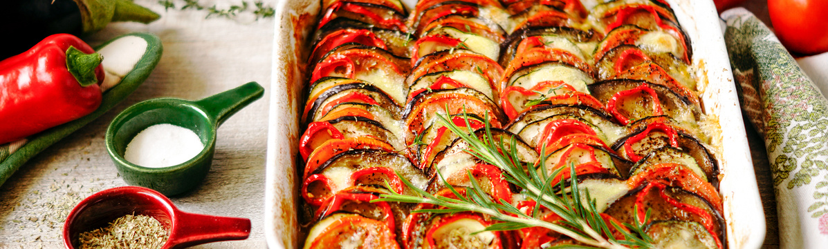 KI generiert: Auflaufform mit geschichtetem Gemüse wie Zucchini, Tomaten und Auberginen, garniert mit Rosmarin.