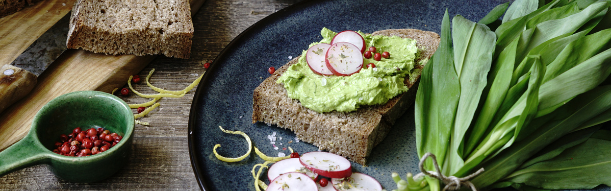 KI generiert: Ein Brotscheibe mit Avocado und Radieschen, daneben Bärlauch und rosa Pfefferkörner.