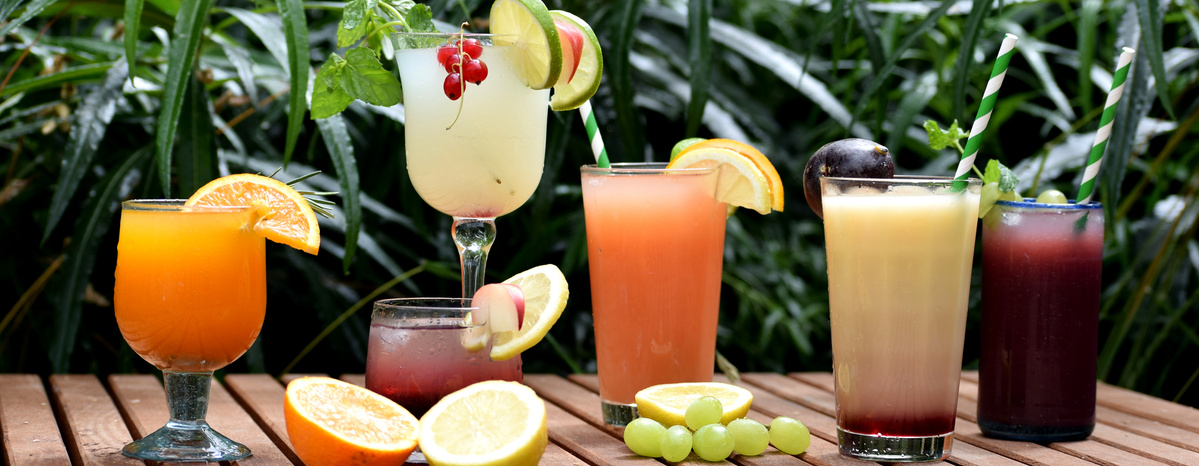 KI generiert: Verschiedene bunte Cocktails auf einem Holztisch mit Früchten und Kräutern als Dekoration.