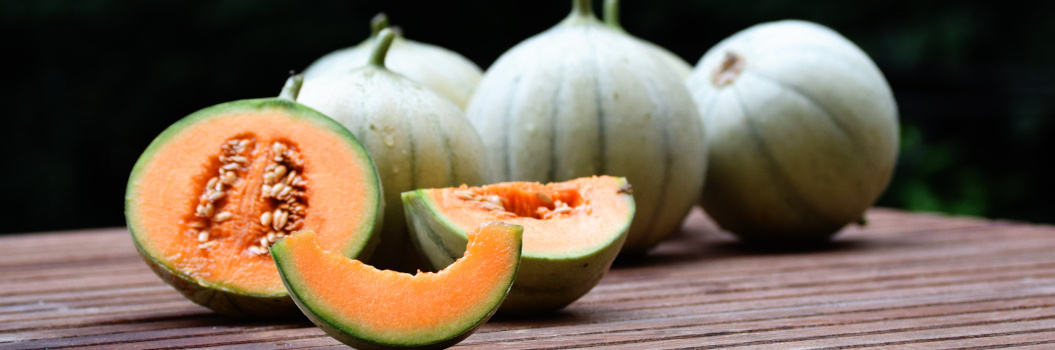 KI generiert: Weiße Melonen und eine aufgeschnittene Melone mit orangefarbenem Fruchtfleisch und Kernen auf einem Holztisch.