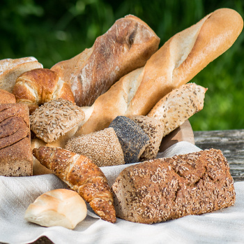 KI generiert: Ein Korb mit verschiedenen Brotsorten, darunter Baguettes und Vollkornbrot, auf einem Holzuntergrund.