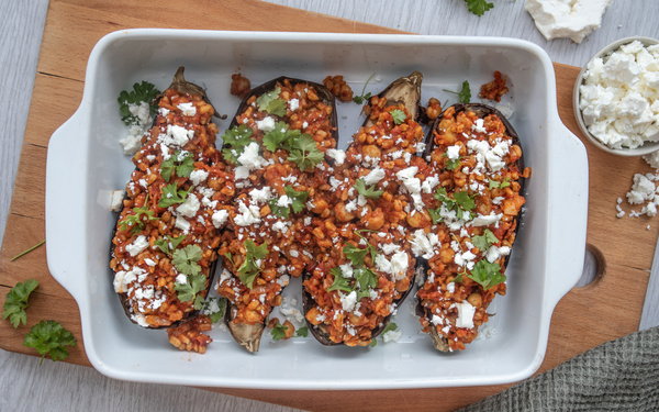 KI generiert: Gefüllte Auberginen mit einer roten Sauce, Petersilie und Feta in einer weißen Auflaufform serviert.