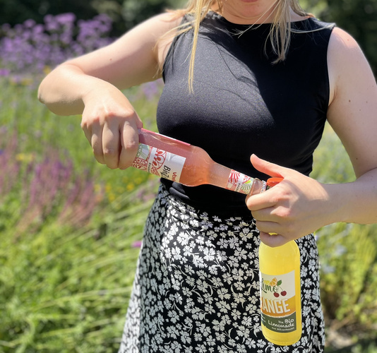 KI generiert: Eine Person hält zwei Bio-Limonadenflaschen im Freien.