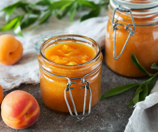KI generiert: Gläser mit Aprikosenmarmelade und frischen Aprikosen, dekoriert mit Blättern auf einem grauen Hintergrund.