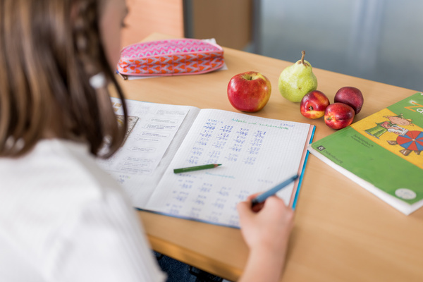 KI generiert: Ein Kind macht Mathe-Hausaufgaben, mit Obst und einem Buch auf dem Tisch.
