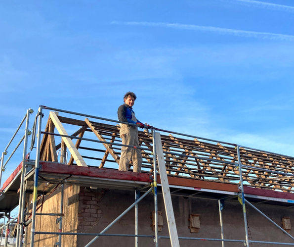 KI generiert: Eine Person steht auf einem Baugerüst vor einem Dachstuhl unter blauem Himmel.