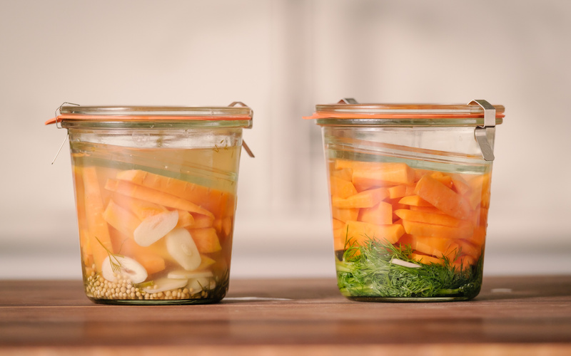 KI generiert: Zwei Einmachgläser mit eingelegtem Gemüse, darunter Karotten, Knoblauch und Dill.