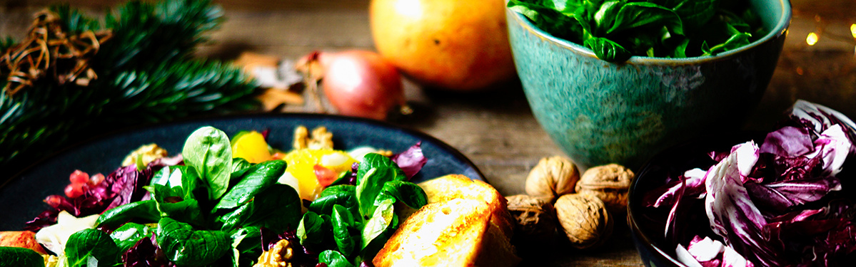 KI generiert: Das Bild zeigt einen frischen Salat auf einem Teller, dekoriert mit verschiedenen Zutaten wie Nüssen, Granatapfelkernen und Brotscheiben. Im Hintergrund stehen weitere Schüsseln mit Salat und ein Granatapfel.