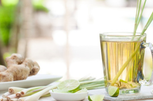 KI generiert: Ein Glas mit Tee und Zitronengras, daneben Ingwer und Limettenstücke.