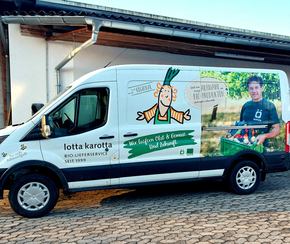 KI generiert: Ein Lieferwagen von "lotta karotta", bewirbt Bio-Obst und Gemüse. Text: "Wir liefern Obst & Gemüse. Und Zukunft."