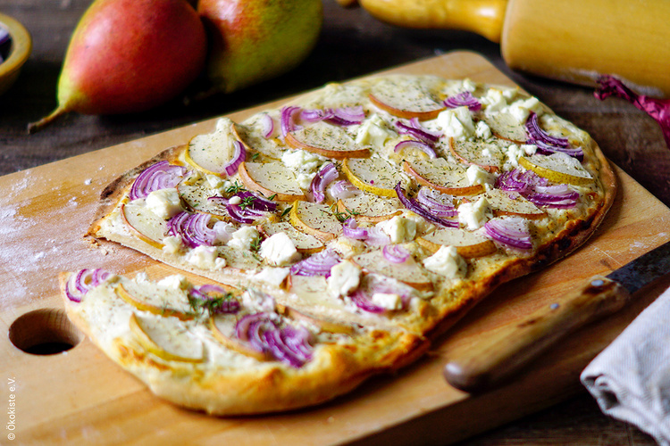 KI generiert: Ein Flammkuchen mit roten Zwiebeln und Birnen auf einem Holzbrett.
