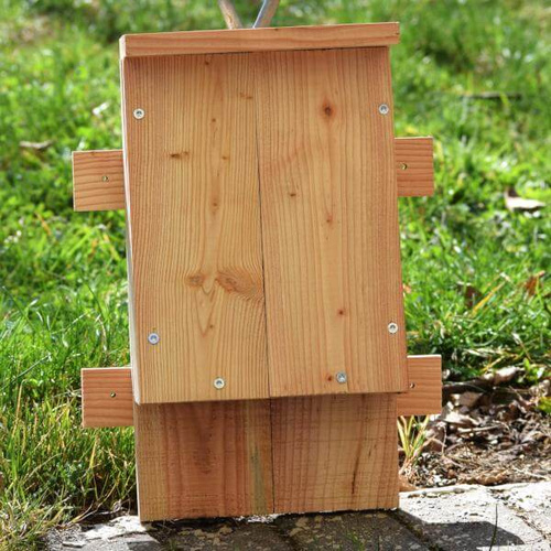 KI generiert: Ein ökologisch anmutender Nistkasten aus Holz steht auf Bodenplättchen im Garten.