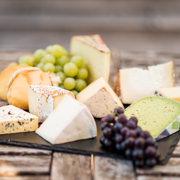 KI generiert: Eine Auswahl verschiedener Käsesorten und Trauben auf einem Holzbrett.