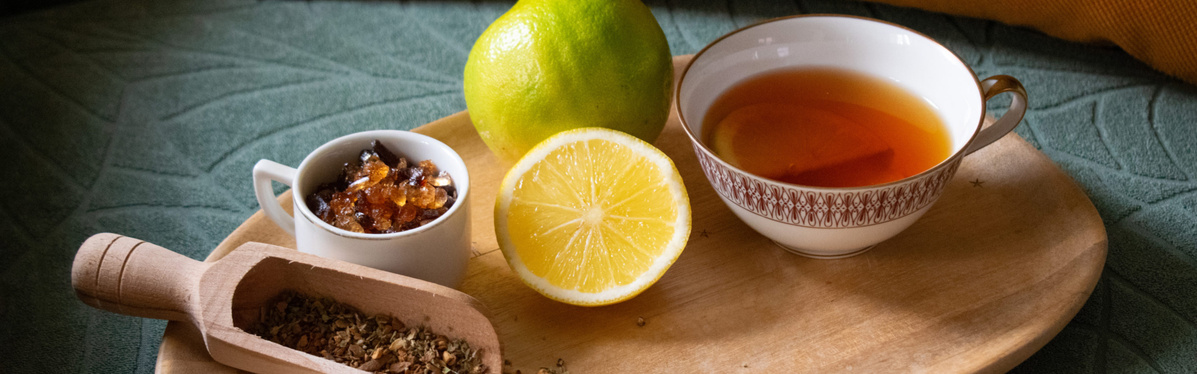 KI generiert: Eine Tasse Tee mit einer halben Zitrone, Kandiszucker und Kräutern auf einem Holzteller.