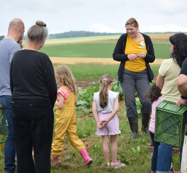 KI generiert: Eine Gruppe von Erwachsenen und Kindern steht auf einem Feld, eine Frau spricht zu ihnen.