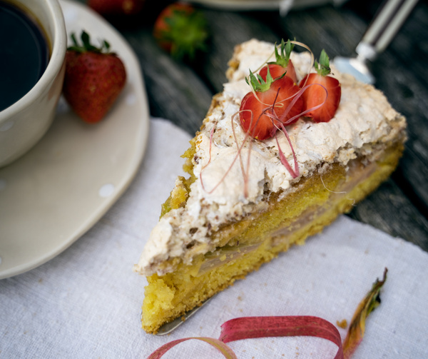 KI generiert: Ein Stück Kuchen mit Sahne und Erdbeeren auf einem Tisch, neben einer Tasse Kaffee und einer Erdbeere.