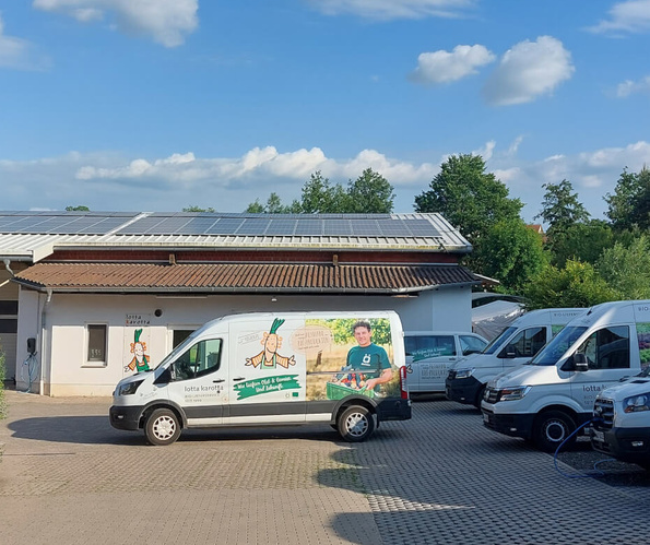 KI generiert: Mehrere Lieferwagen auf einem Hof mit Solarpanel-Dach, einer trägt den Text "lotta karotta".