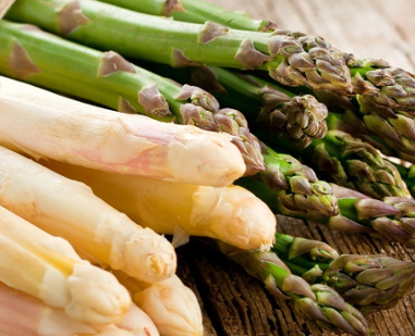 KI generiert: Grüner und weißer Spargel liegen nebeneinander auf einem Holztisch.