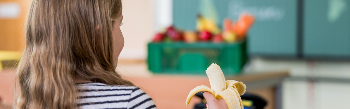 KI generiert: Ein Kind hält eine geschälte Banane. Im Hintergrund steht eine Kiste mit Obst.
