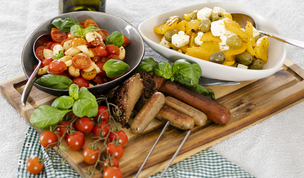 KI generiert: Verschiedene Antipasti und Würstchen auf einem Holzbrett, dekoriert mit frischen Basilikumblättern.