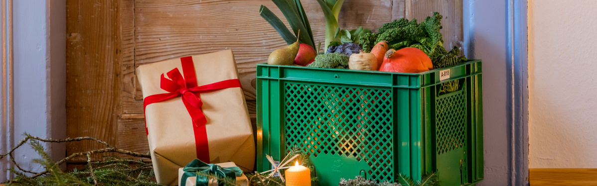 KI generiert: Grüne Kiste mit buntem Gemüse, Geschenke daneben; stimmungsvolle Weihnachtsdekoration mit Kerze.