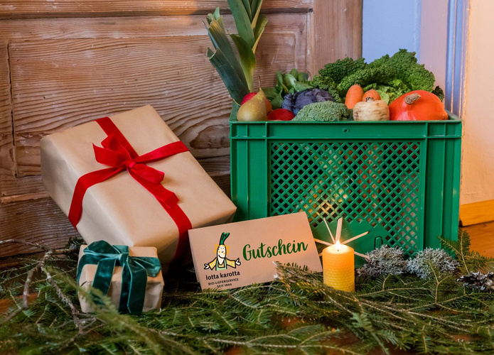 KI generiert: Eine Gemüsekiste mit Weihnachtsgeschenken; Text: "Gutschein lotta karotta BIO-LIEFERSERVICE".