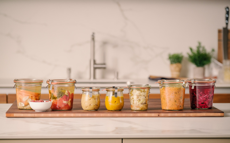 KI generiert: Eine Reihe von gefüllten Einmachgläsern auf einem Holzbrett in einer Küche.