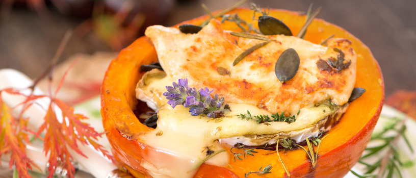 KI generiert: Gefüllter Kürbis mit geschmolzenem Käse, Kräutern und Kürbiskernen, dekoriert mit Lavendel.