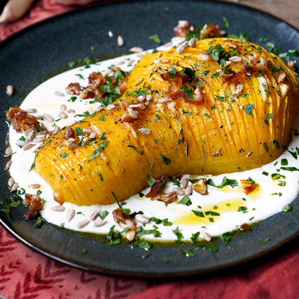 KI generiert: Ein gebackener Butternut Kürbis auf Sahnesoße mit Kräutern und Nüssen garniert auf einem dunklen Teller.