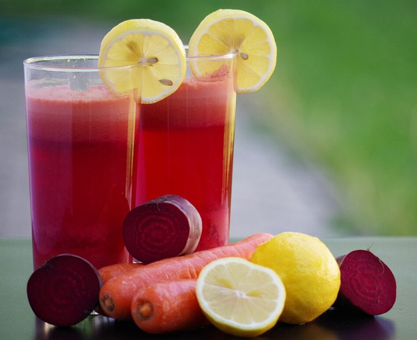 KI generiert: Zwei Gläser roten Saftes mit Zitronenscheiben, umgeben von Karotten, Rote Bete und Zitronen.