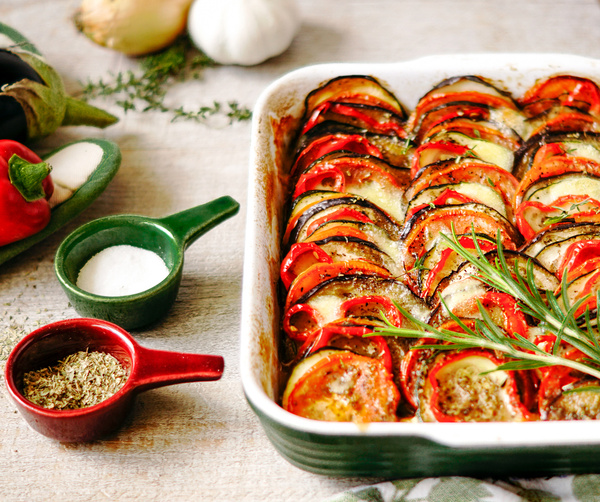 KI generiert: Ofenratatouille in einer Auflaufform, umgeben von Gewürzen und Gemüse.