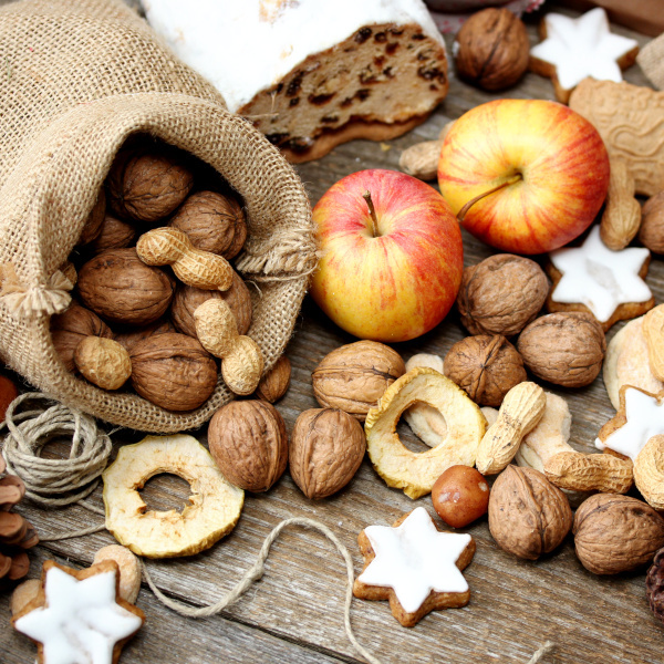 KI generiert: Nüsse, Äpfel, Trockenfrüchte, Gebäck und ein Sack auf einem Holztisch. Weihnachtsstimmung mit Stollen und Keksen.