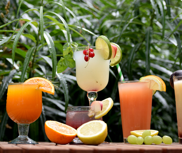 KI generiert: Bunte Cocktails mit Früchten dekoriert vor grünen Pflanzen.