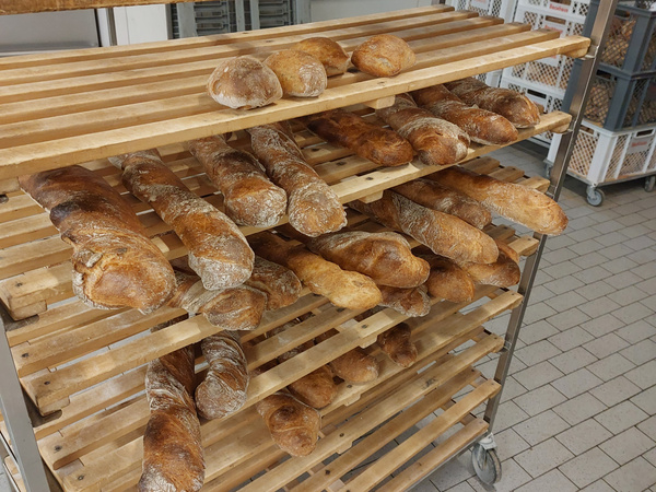 KI generiert: Ein Wagen voller frisch gebackener Brote und Baguettes auf Holzregalen.