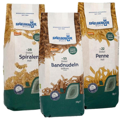 KI generiert: Drei Packungen Spielberger Mühle Bio-Dinkel-Nudeln: Spiralen, Bandnudeln, Penne; verpackt in Papier.