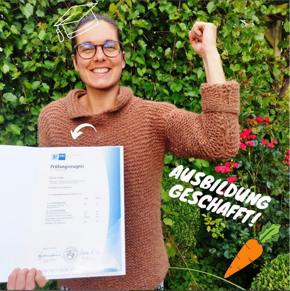 Maria hält ihr IHK-Abschlusszeugnis in der Hand, die andere Hand zu einer Sieger-Faust- Pose gehoben