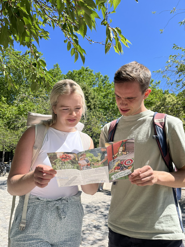 KI generiert: Zwei Personen schauen sich Prospekte an, während sie in einem sonnigen Park stehen. Text: „ÖkoKiste“.