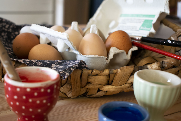 KI generiert: Eier in einem Korb mit Farbgläsern und Pinseln, bereit zum Bemalen.