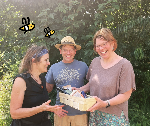 KI generiert: Drei Personen stehen draußen, einer hält einen Geschenkkorb. Zeichnungen von Bienen sind eingefügt.
