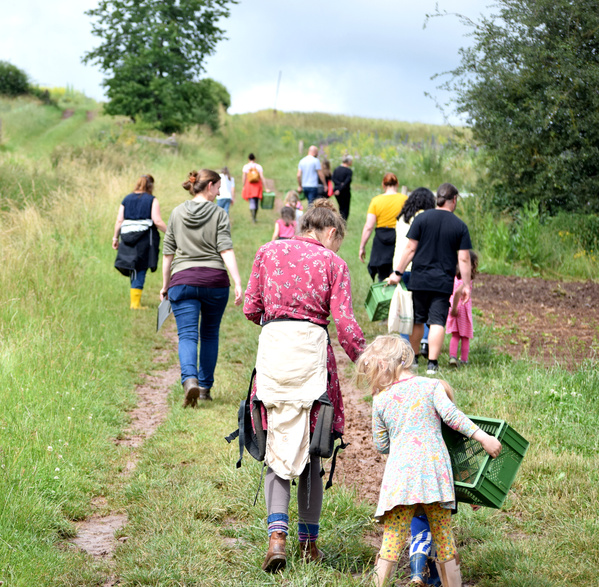 KI generiert: Eine Gruppe von Menschen geht draußen über einen Feldweg und trägt grüne Kisten.
