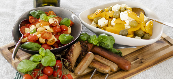KI generiert: Verschiedene Salate mit Tomaten, Paprika und Oliven, dazu Würstchen auf einem Holzbrett angerichtet.