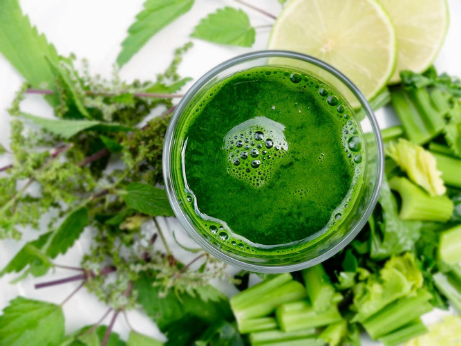 KI generiert: Grüner Smoothie in einem Glas, umgeben von grünem Gemüse und Limettenscheiben.