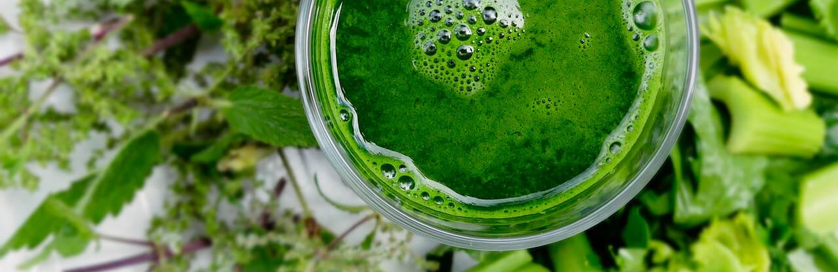 KI generiert: Ein Glas grüner Smoothie umgeben von frischem Gemüse und Kräutern.
