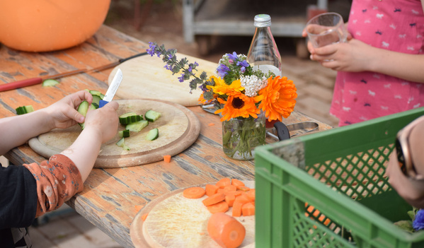 KI generiert: Kinder schneiden Gemüse auf einem Tisch, Vase mit Blumen daneben.