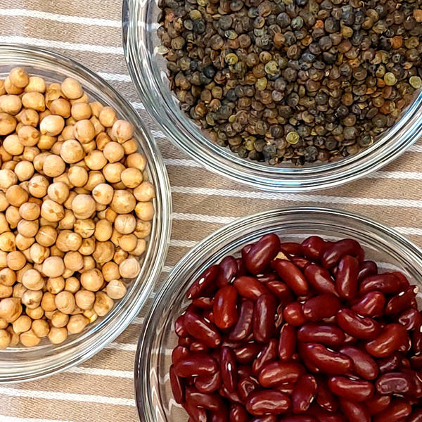 KI generiert: Drei Glasschalen mit Kichererbsen, grünen Linsen und Kidneybohnen auf gestreiftem Tuch.