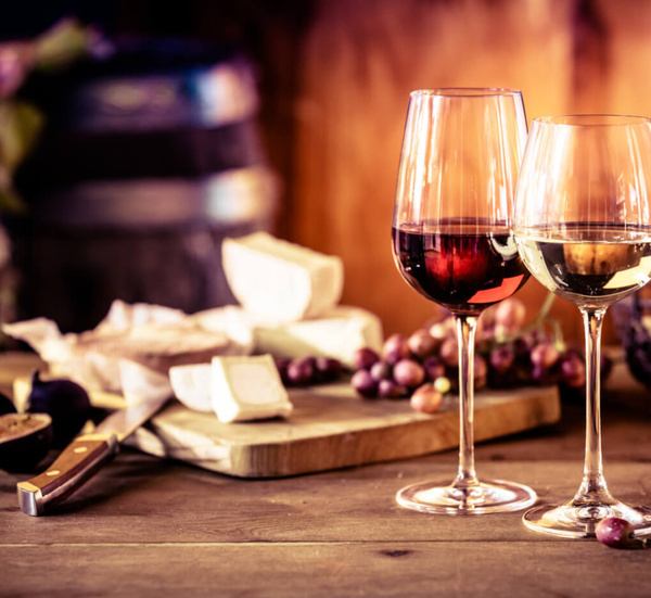 KI generiert: Zwei Weingläser, Käse und Trauben auf einem Tisch.