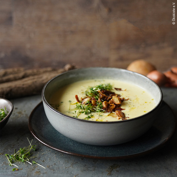 KI generiert: Eine Schüssel cremige Suppe, garniert mit Kräutern und Pilzen. Text: "© ökokiste e.V."