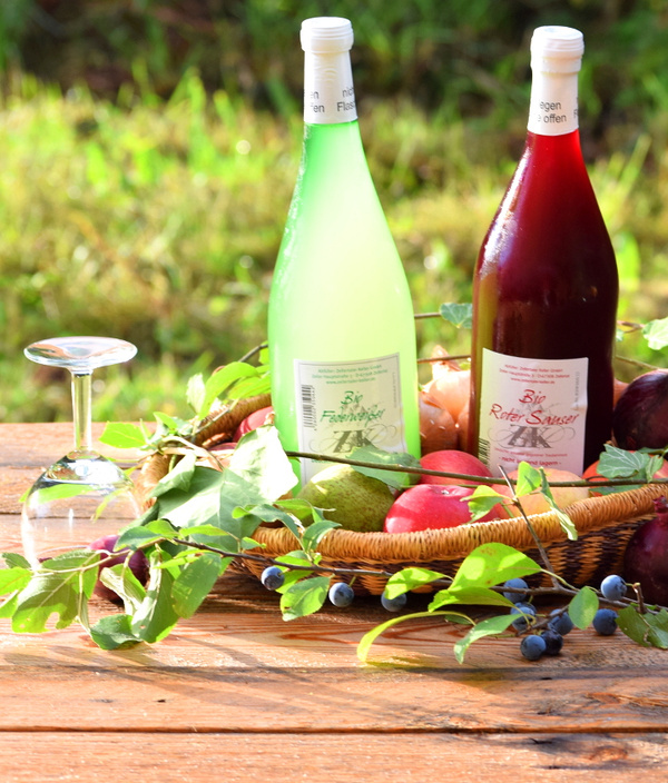 KI generiert: Zwei Weinflaschen im Korb mit Früchten auf Holztisch im Freien.